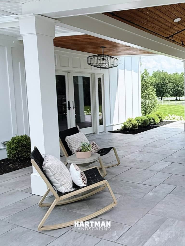 Covered patio with stone paving, rocking chairs, and open landscape — a Hartman Landscaping project